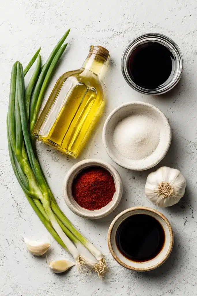 Flat lay of Asian cooking ingredients including oil, soy sauce, vinegar, chili powder, salt, garlic, and green onion on white tile background