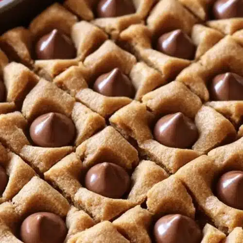 Close-up of peanut butter blossom bars topped with chocolate drops in a baking pan