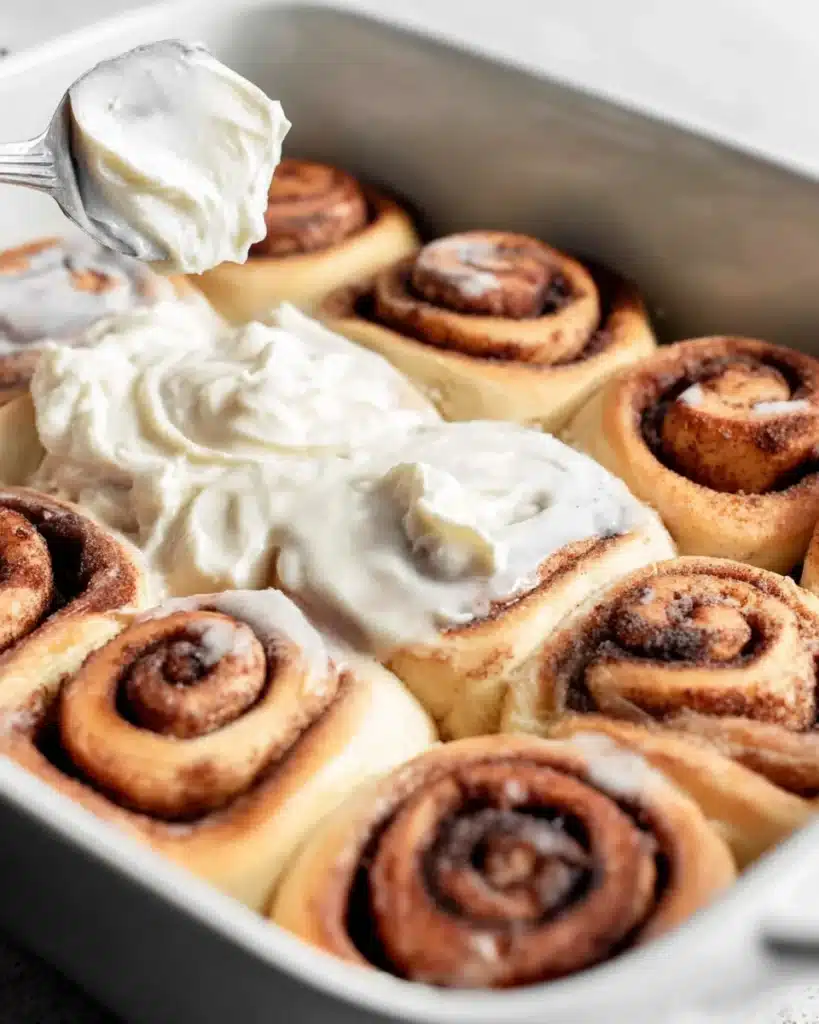 spreading cream cheese icing on homemade cinnamon rolls