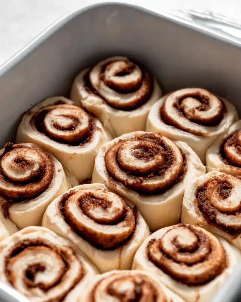 unbaked homemade cinnamon rolls with perfect swirls in white pan