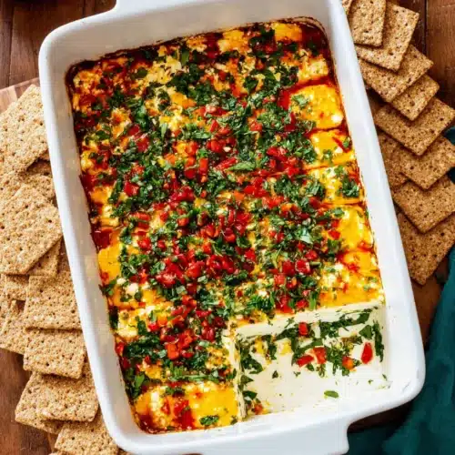 layered marinated cheese with herbs and peppers in a white dish