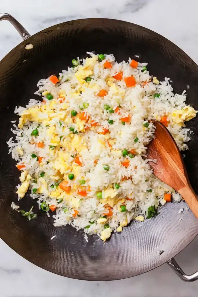 egg fried rice being mixed with eggs veggies and rice in wok