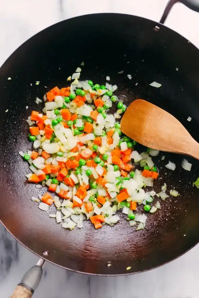 sautéed onions carrots and peas in wok with wooden spoon