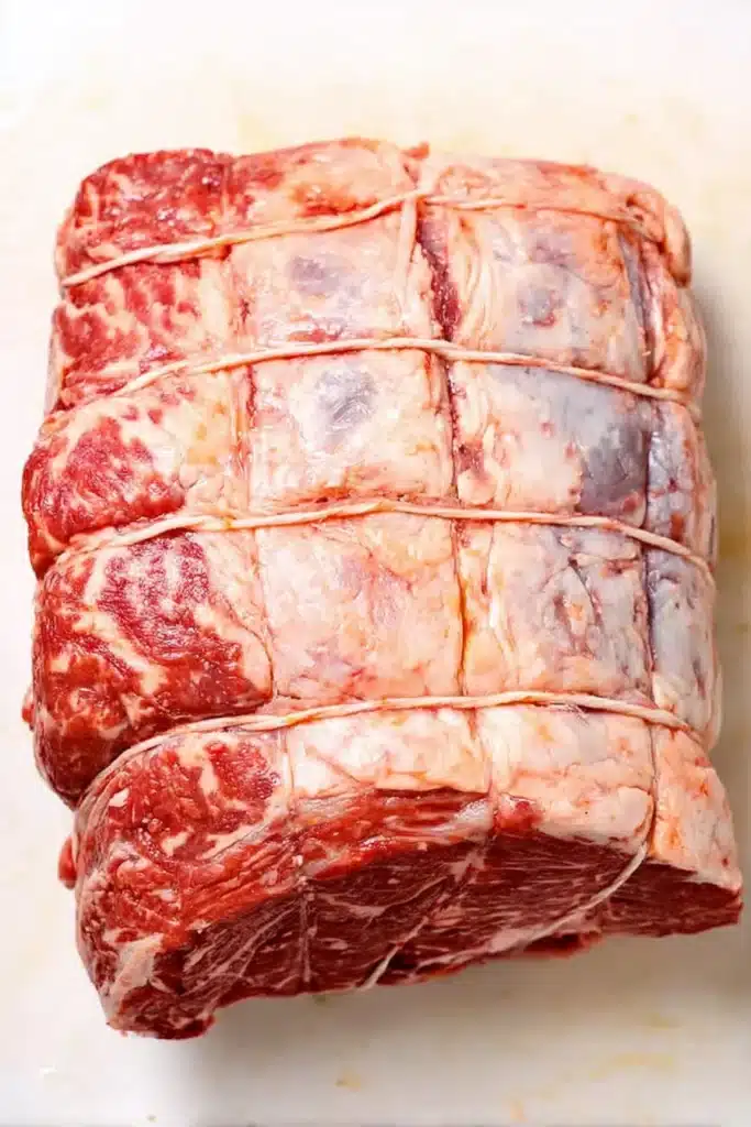 raw prime rib roast tied with twine on white cutting board