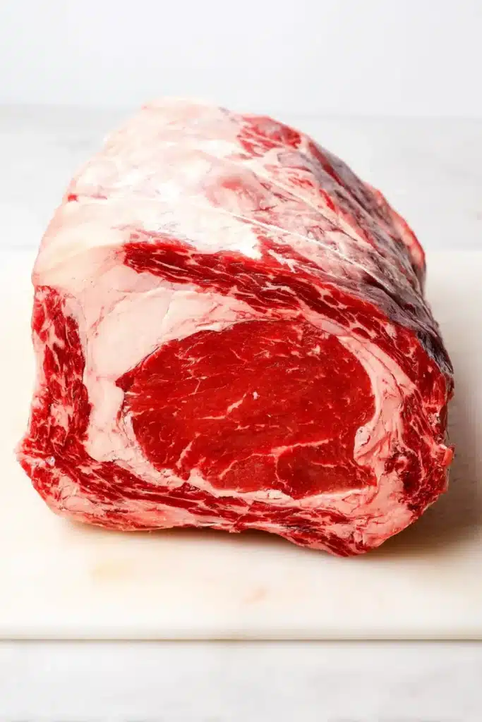 raw prime rib roast with thick fat cap and marbling on cutting board