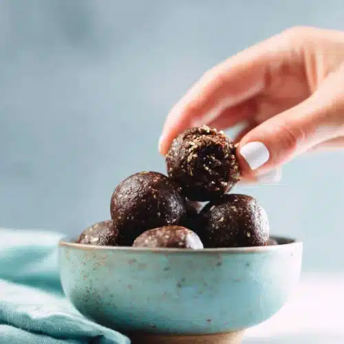 A hand reaching for chocolate energy balls, a nutritious snack.