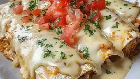 Queso chicken enchiladas topped with cheese and sauce in a baking dish
