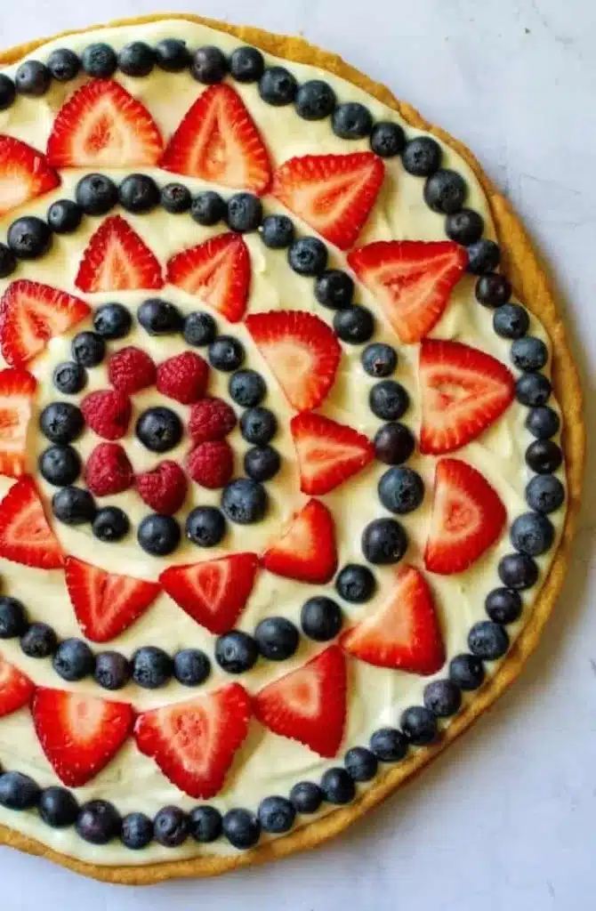 Fourth of July fruit pizza topped with fresh berries and whipped cream.