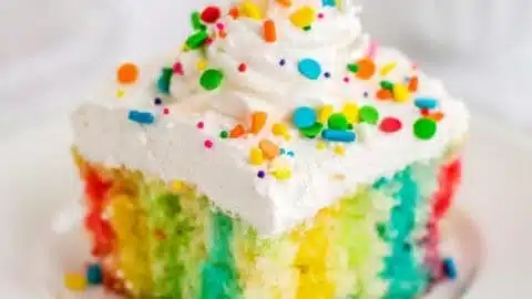 Rainbow Jello Poke Cake with colorful layers and whipped cream on top.