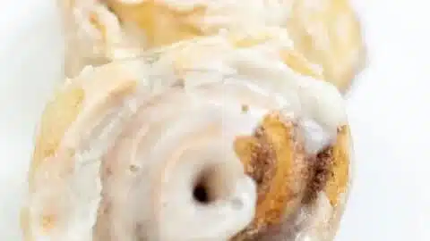 Freshly baked sourdough cinnamon rolls topped with creamy icing on a plate.